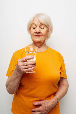 Portrait of an old friendly woman holding a glass of water health close-up emotionsの写真素材