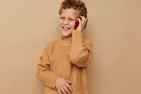 Cheerful boy talking on the phone on a beige backgroundの写真素材