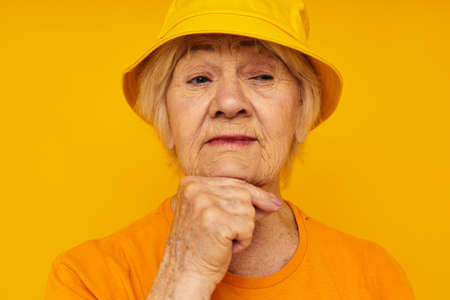 Portrait of an old friendly woman in casual t-shirt yellow panama yellow backgroundの写真素材