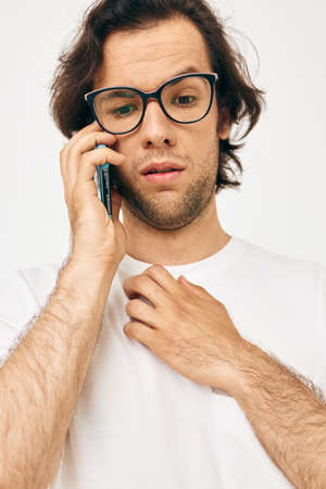 Attractive man in a white T-shirt communication by phone light backgroundの写真素材
