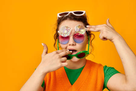 portrait of a young woman multicolored sunglasses on face posing grimace yellow background unalteredの写真素材