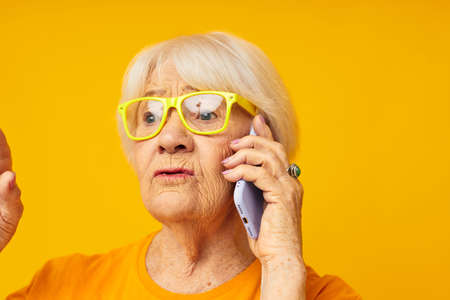 Portrait of an old friendly woman fun talking on the phone yellow background