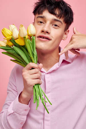 portrait of a young man in a pink shirt with a bouquet of flowers gesturing with his hands Lifestyle unalteredの写真素材
