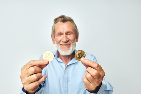 Portrait elderly man in a blue shirt bitcoins on the face light backgroundの写真素材