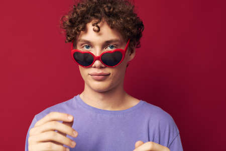 cute red-haired guy hand gestures heart shaped glasses posing red backgroundの写真素材