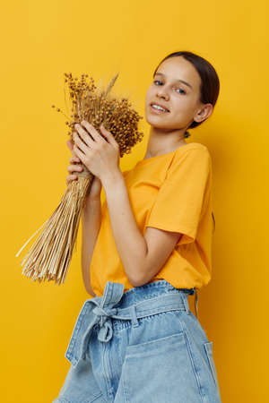 young beautiful woman fashion in yellow t-shirt dried flowers bouquet posing yellow background