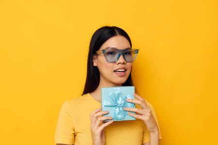 Portrait Asian beautiful young woman with a gift in glasses holiday yellow background unalteredの写真素材