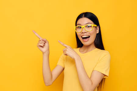 Charming young Asian woman in yellow t-shirts with glasses posing fashion yellow background unalteredの写真素材