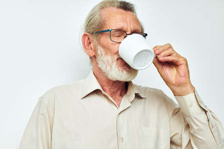 elderly man drinking from a mug on a white background and smiling