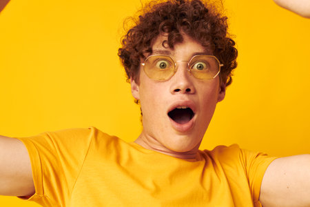 Young curly-haired man yellow t-shirt glasses fashion hand gestures isolated background unalteredの写真素材