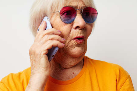 elderly woman in casual t-shirt sunglasses talking on the phone isolated backgroundの写真素材