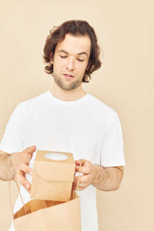 handsome man in a white T-shirt with paper bag beige background