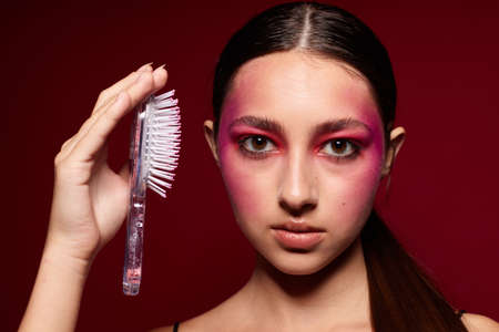 fashionable woman with a comb bright makeup posing black jersey pink background unaltered