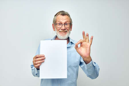 Senior grey-haired man in a blue shirt and glasses a white sheet of paper cropped viewの写真素材