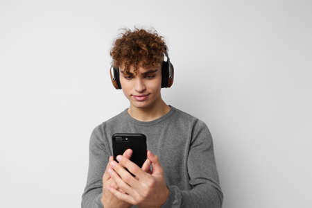 Attractive man with a phone in hand listening to music in headphones light backgroundの写真素材
