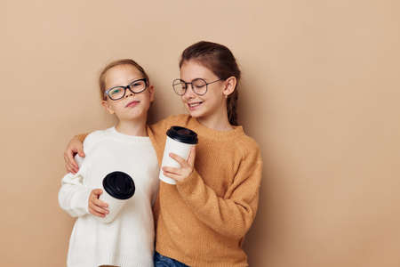 two little funny girls a glass with a drink beige backgroundの写真素材