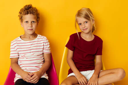 Small children childhood sitting on chairs together on colored backgroundの写真素材