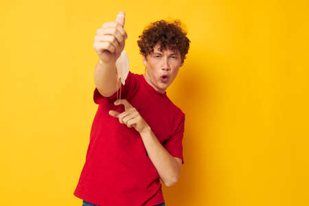 portrait of a young curly man in a red t-shirt medical mask protection yellow background unaltered