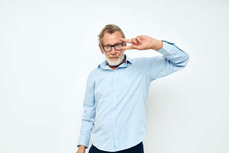 Portrait of happy senior man in blue shirts gestures with his hands light background