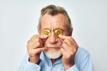 Senior grey-haired man cryptocurrency bitcoin face close up investment light backgroundの写真素材