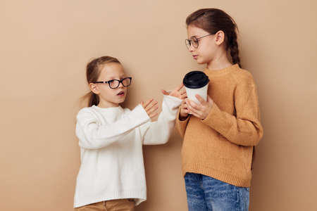 two little girls disposable glasses posing beige backgroundの写真素材
