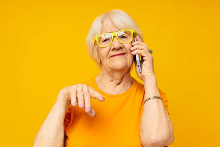 Photo of retired old lady happy lifestyle in yellow t-shirts with phone isolated backgroundの写真素材
