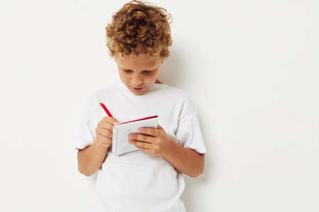 A cheerful boy with curly hair draws in a notebook with a pencilの写真素材
