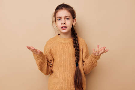 Portrait of happy smiling child girl long pigtail beige sweater grimace beige backgroundの写真素材