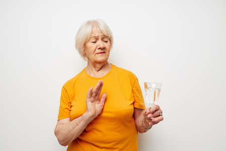 smiling elderly woman in casual t-shirt glasses glass of water isolated background