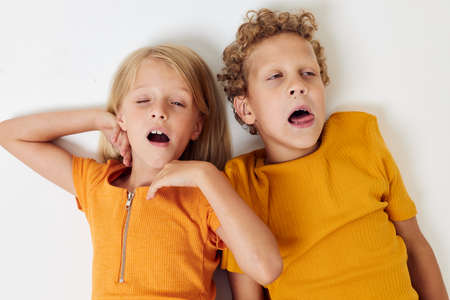 boy and girl lie on a white background in yellow t-shirts emotionsの写真素材