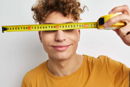 handsome guy measuring tape measure in yellow t-shirt light backgroundの写真素材