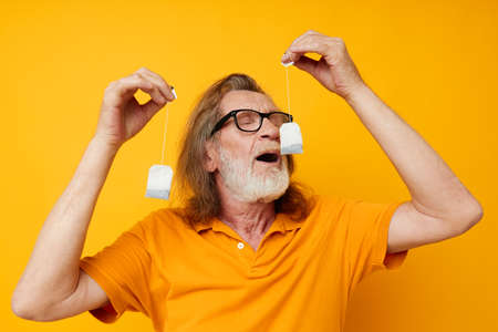 elderly man with tea bags yellow background posing