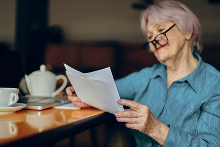 Senior woman with glasses sits at a table in front of a laptop Freelancer works unalteredの写真素材
