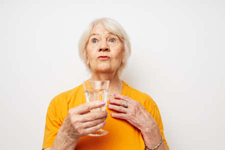 smiling elderly woman in yellow t-shirts a glass of water in his hands cropped viewの写真素材
