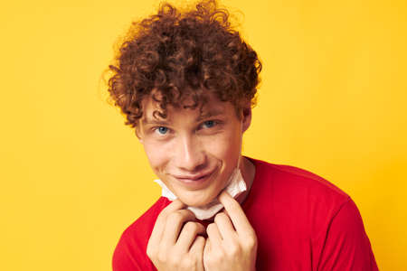 guy with red curly hair in a red t-shirt medical mask protection yellow background unalteredの写真素材