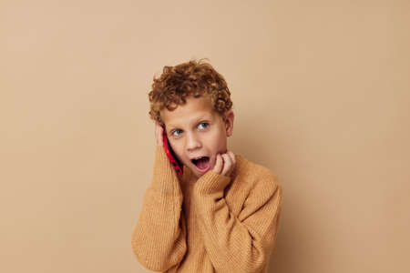 curly boy talking on the phone posing beige backgroundの写真素材