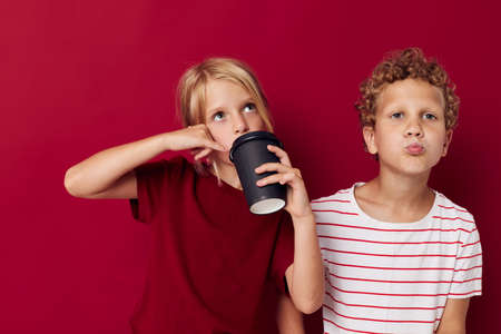 boy and girl are standing next to a disposable glass with a drink red backgroundの写真素材