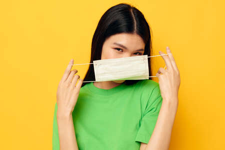 Portrait Asian beautiful young woman in green t-shirt medical mask protection yellow background unalteredの写真素材