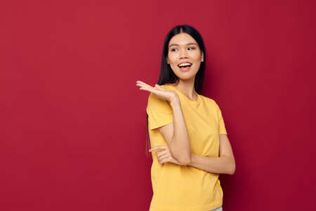 Charming young Asian woman yellow casual t shirt smile posing red background unalteredの写真素材