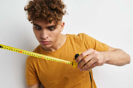 handsome guy measuring tape measure in yellow t-shirt light backgroundの写真素材
