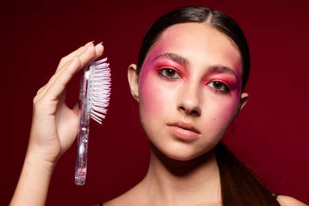 Young beautiful woman with a comb in hand bright makeup posing fashion emotions pink background unalteredの写真素材