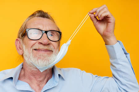 Portrait elderly man in medical mask protection yellow background