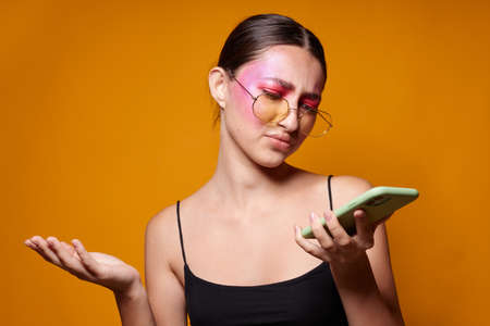 Young beautiful woman with a phone in hand bright makeup posing fashion emotions yellow background unalteredの写真素材