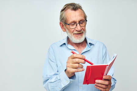 Senior grey-haired man with red notebook and pen light backgroundの写真素材