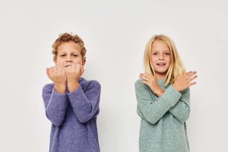 Little boy and girl in multi-colored sweaters posing for fun light backgroundの写真素材