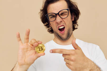 Cheerful man in a white T-shirt with Bitcoin cryptocurrency beige background