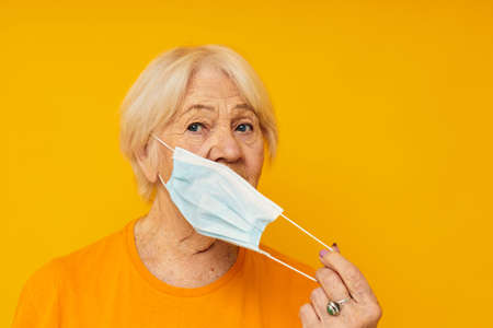 Photo of retired old lady in yellow t-shirts in medical masks close-up emotionsの写真素材