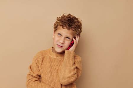 Cheerful boy talking on the phone on a beige background
