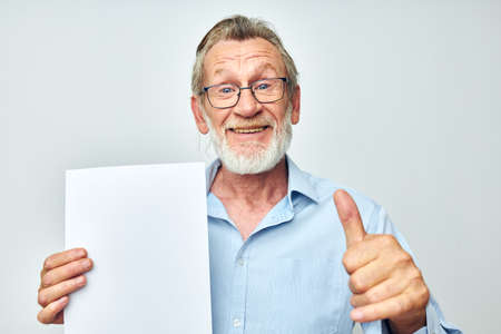 Senior grey-haired man blank sheet of paper gesture hands smile light background