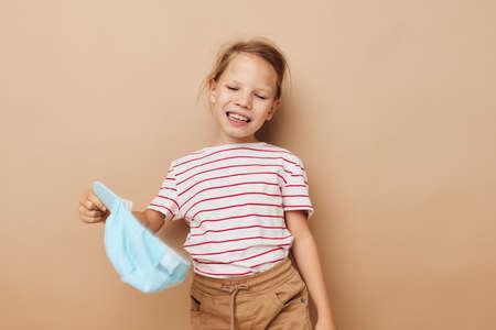 Portrait of happy smiling child girl in blue caps striped t-shirt emotions beige backgroundの写真素材